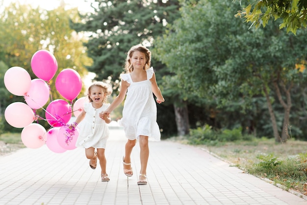 Meninas felizes segurando balões correndo no parque ao ar livre sobre o fundo da natureza Celebração da festa de aniversário