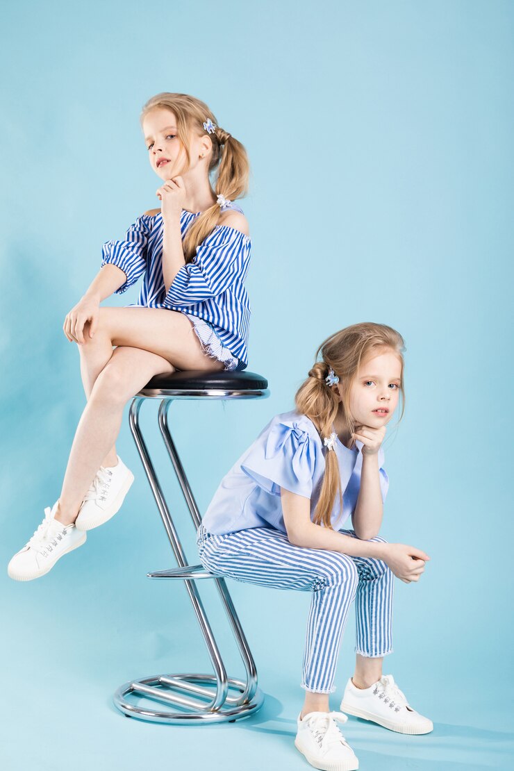 Foto meninas gêmeas em roupas azuis claras estão posando perto de um banquinho em um azul.