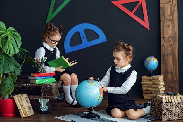 Meninas inteligentes lendo livros e examinando o globo na escola