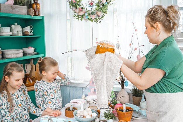 Meninas irmãs mãe à mesa com decoração de Páscoa Celebração na cozinhaTablescape para férias de Páscoa em casa Refeição de comida festiva tradicional religiosa da família Orelhas de coelho divertidas de bolo de ovos coloridos