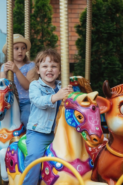 Foto meninas irmãs no parque de diversões se divertem andando nos carrosséis