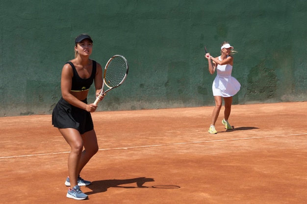 Meninas jogando uma partida de duplas de tênis em uma quadra de saibro