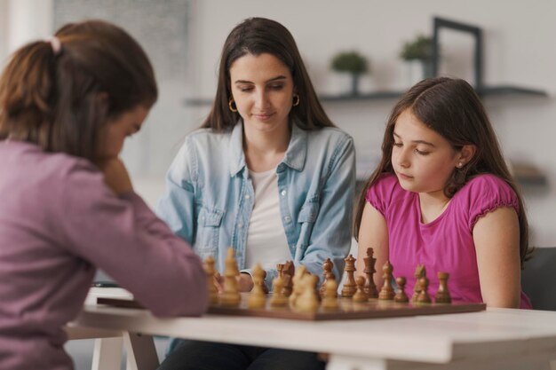 Foto meninas jogando xadrez juntas em casa sua mãe está sentada ao lado deles e assistindo