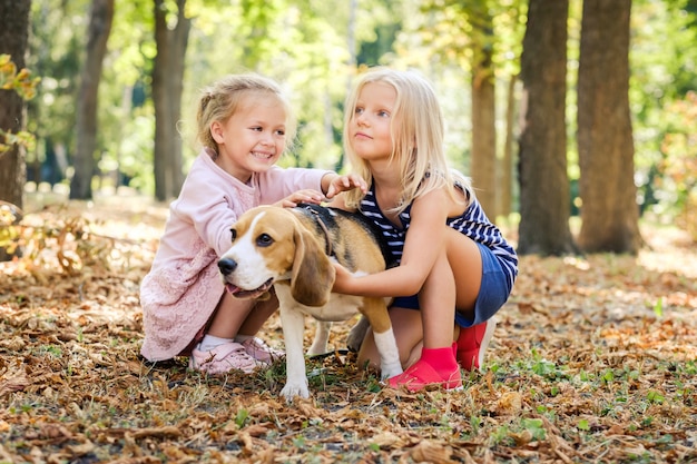 Meninas loiras sorridentes sentar abraçando cachorro beagle