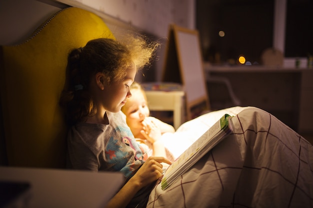 Meninas melhores amigas lêem conto de fadas antes de dormir. Melhores livros para crianças. Irmãs ler o livro na cama. Tradição familiar.