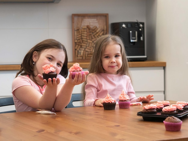 Meninas na cozinha na mesa segurando cupcakes com uma tampa de creme rosa nas mãos