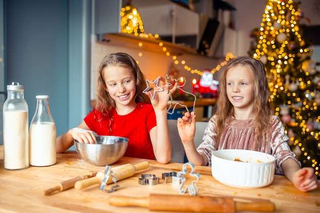 Meninas que fazem a casa de gengibre de Natal na lareira na sala de estar decorada.