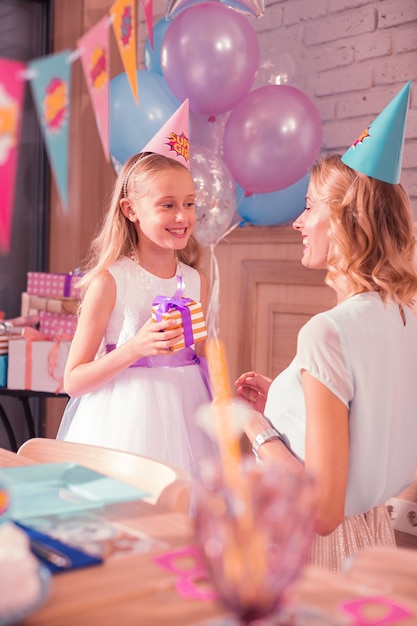 Meninas sorridentes. Menina alegre e sua mãe sorrindo enquanto usavam chapéus de festa lindos e esperavam pelos convidados