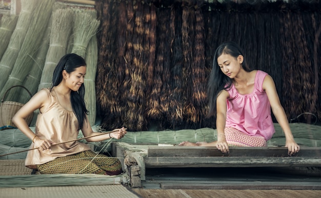 Meninas tailandesas que trabalham matérias têxteis com o papiro a esteira.