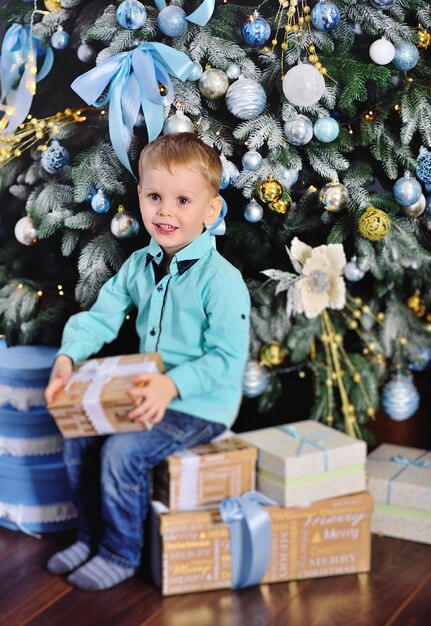 Menino abre caixas com presentes debaixo da árvore de Natal e sorri