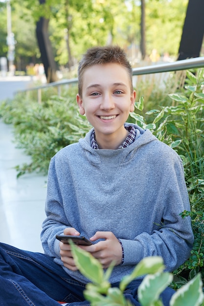 Menino adolescente criança com telefone móvel se senta e sorri. aprendizagem online, educação à distância, ensino em casa.