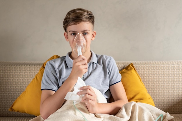 Menino adolescente doente com um inalador Criança insalubre fazendo inalação em casa ela usa nebulizador e inalador para o tratamento sentado no sofá em casa Asma inalador nebulizador vapor gripe ou resfriado
