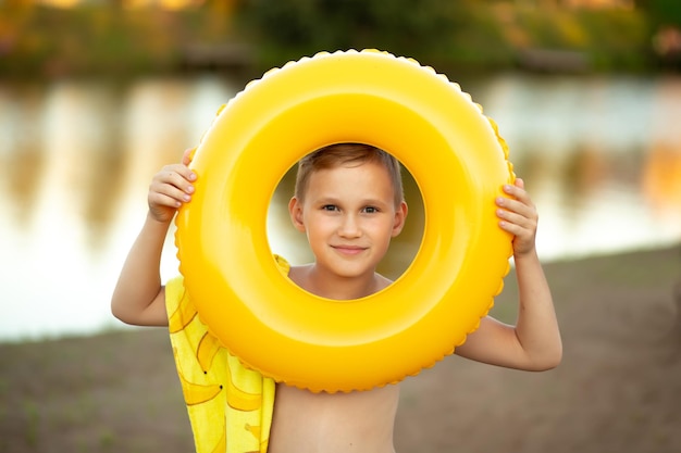 Menino adolescente feliz com boia salva-vidas de anel de natação amarelo perto do lago do rio ou conceito de férias de lagoa