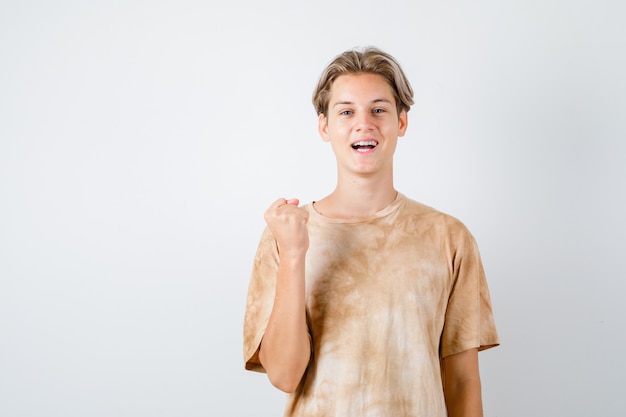 Menino adolescente mostrando o gesto do vencedor em t-shirt e olhando feliz, vista frontal.