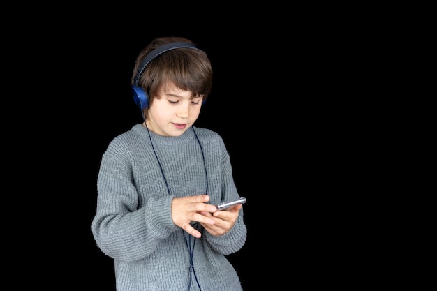 Menino adolescente ouvindo música no player com fones de ouvido em fundo preto Amante da música Criança escolhendo uma nova música em seu smartphone