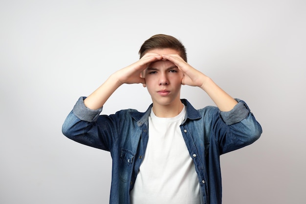 Foto menino adolescente segurando as mãos em sua testa e olhando para longe para o futuro fundo branco com espaço de cópia