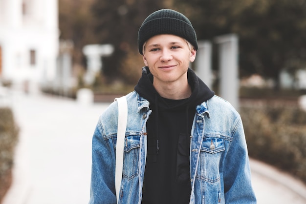 Menino adolescente sorridente usando um boné de malha preta com capuz e jaqueta jeans