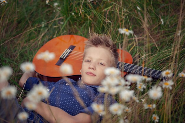 Menino adorável com a guitarra, relaxando no parque. Garoto deitado em uma grama no dia de verão