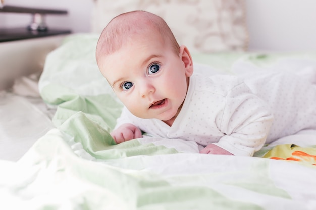 Menino adorável com olhos grandes e cílios longos. bebê fofo deitado de bruços e olhando para a câmera,