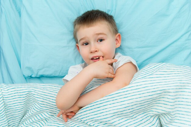 Menino adorável pensativo na camisa branca deita na cama