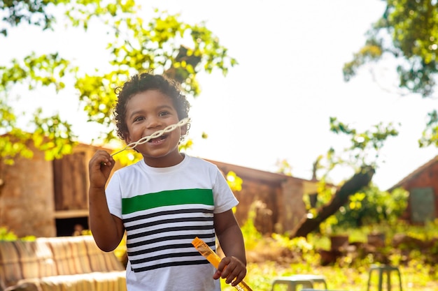 Foto menino africano feliz brincando com bolhas de sabão na natureza