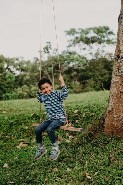 Menino afro-americano balançando em um balanço na natureza