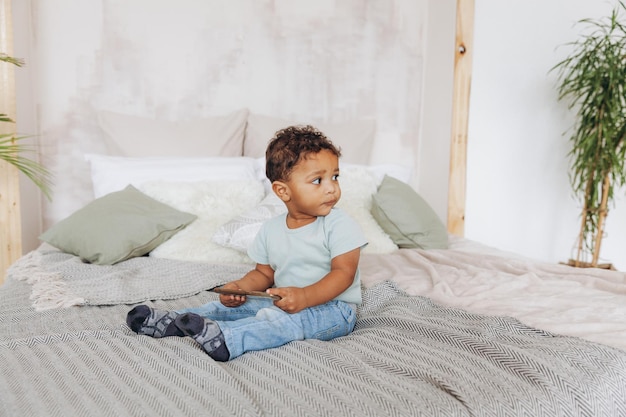 Menino afro-americano bonitinho com smartphone em casa na cama criança feliz assistindo desenhos no telefone