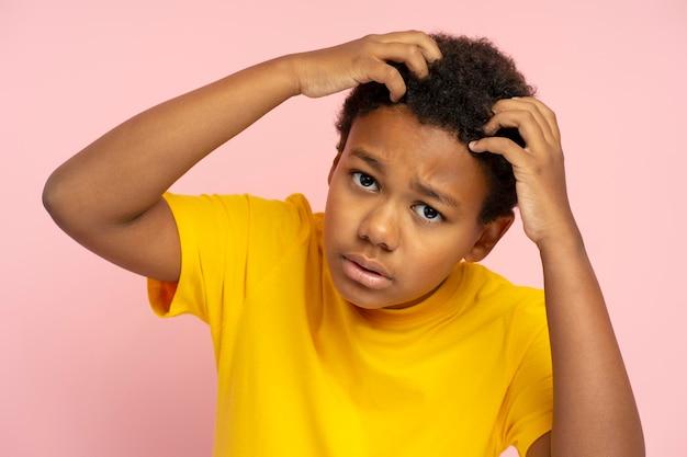 Menino afro-americano chateado olhando no espelho tocando o cabelo isolado no fundo rosa problema de perda de cabelo adolescente triste conceito de tratamento de cuidados com os cabelos