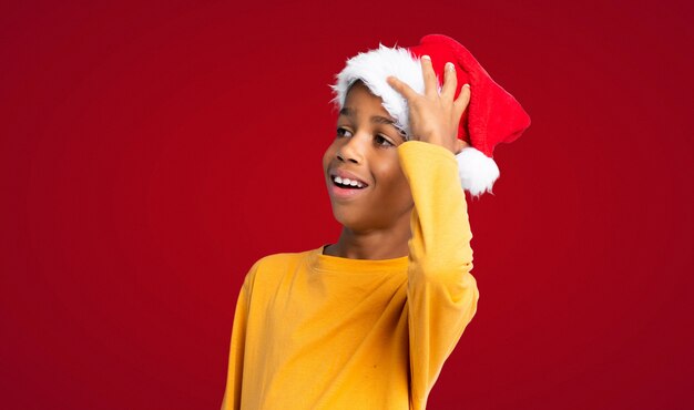 Menino afro-americano com chapéu de Natal percebeu algo e pretendendo a solução sobre parede vermelha