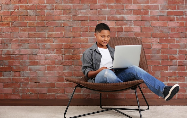 Menino afro-americano com laptop no fundo da parede de tijolos