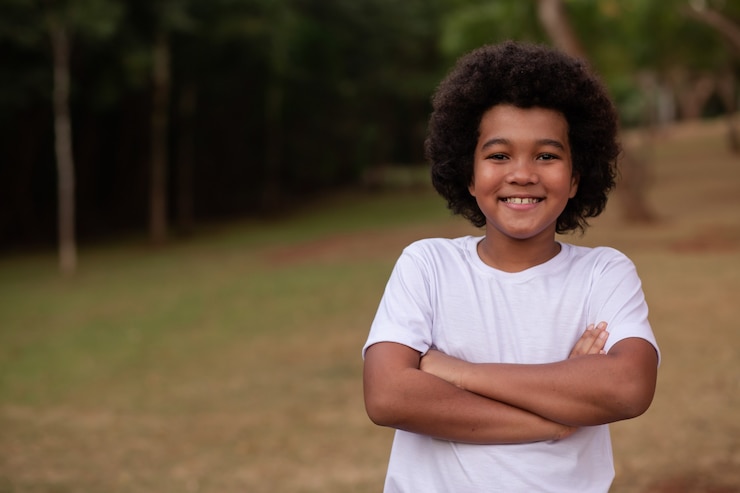 Foto menino afro com os braços cruzados com o parque ao fundo.