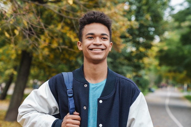 Menino alegre, adolescente caminhando no parque, carregando uma mochila