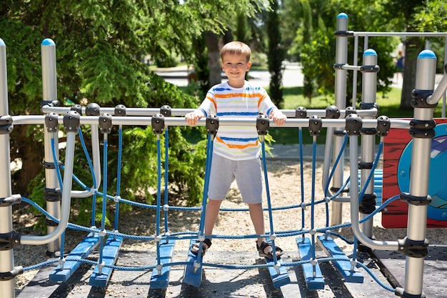 Menino alegre caminha em uma ponte de corda em um playground no parque