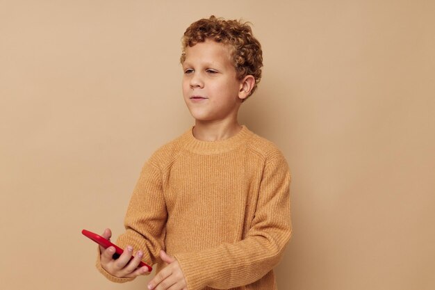 Menino alegre com telefone vermelho nas mãos posando de fundo bege