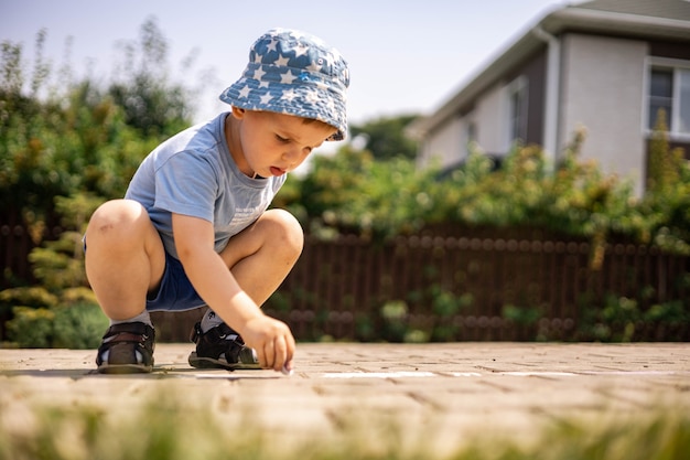 Menino alegre desenhando amarelinha com giz no chão, curtindo uma infância feliz no quintal