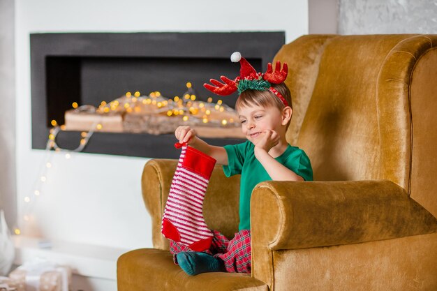 Menino alegre é uma carta para o Papai Noel perto da árvore de Natal. Infância feliz