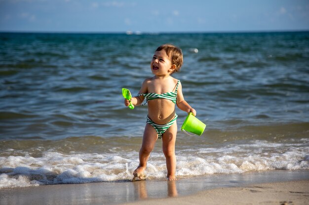 menino alegre feliz brinca nas ondas do mar com um balde e uma pá.