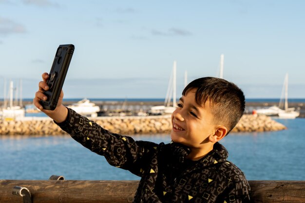 Menino alegre tomando selfie perto do mar