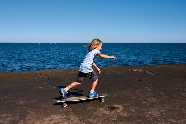 Menino andando de longboard em um cais em dia ensolarado