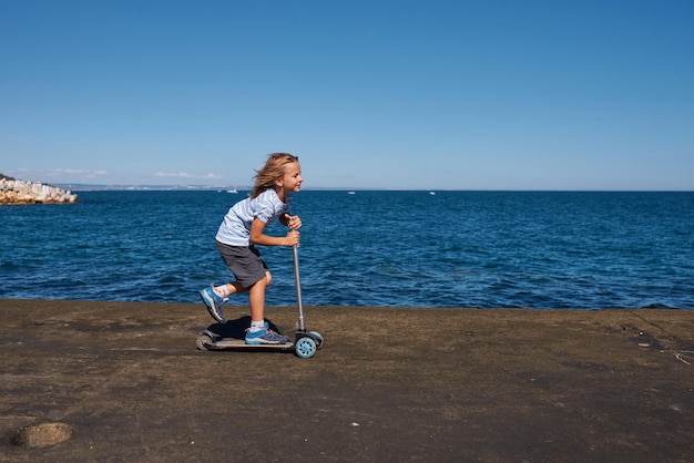 Menino andando de scooter em um cais em dia ensolarado