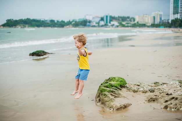 Menino andando na praia perto do mar. Criança bonitinha na praia tropical.