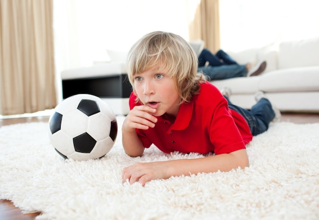 Menino animado assistindo jogo de futebol deitado no chão