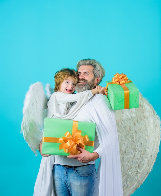 Menino anjo dá um presente para o pai pai feliz fantasiado de anjo com filho pequeno anjo dá um presente