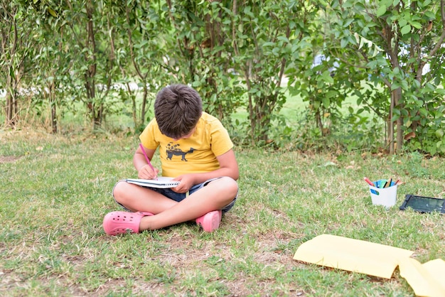 Menino ao ar livre na grama no quintal usando seu computador tablet Educando e brincando