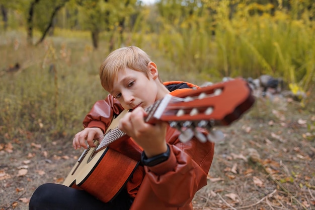 Menino ao ar livre no parque outono tocando guitarra