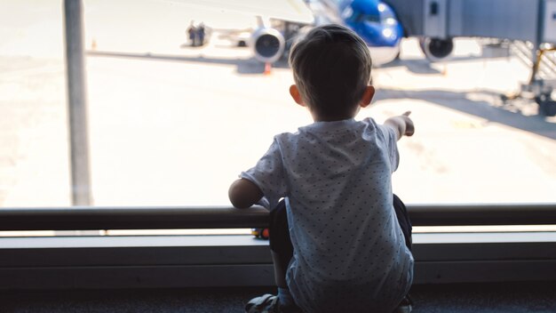 Menino apontando com o dedo no avião no aeroporto.