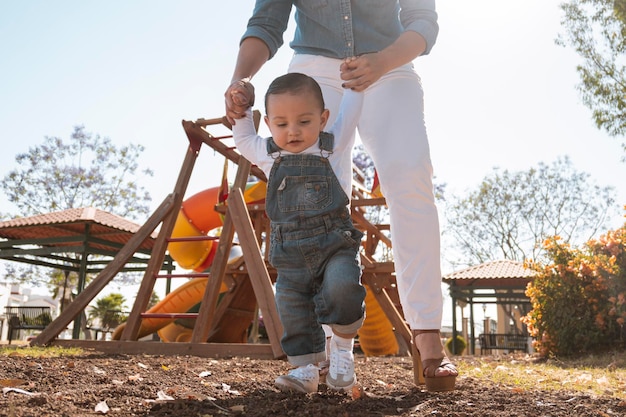 Menino aprende a andar segurando as mãos de sua mãe ao ar livre