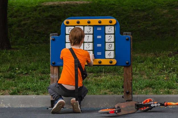 Menino aprende a contar no tabuleiro de jogo com cubos com números e símbolos matemáticos no playground