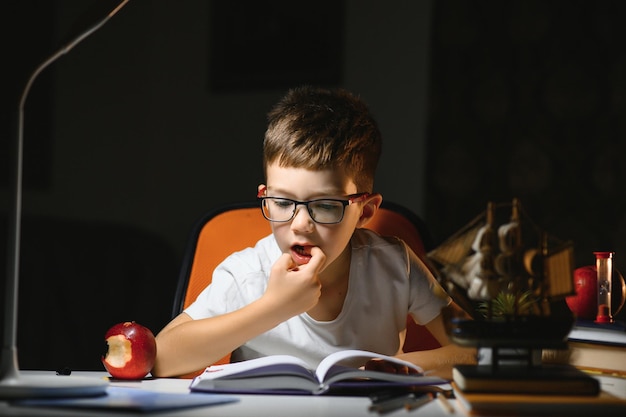 Menino aprende lições em casa, sentado à mesa à luz de um abajur.