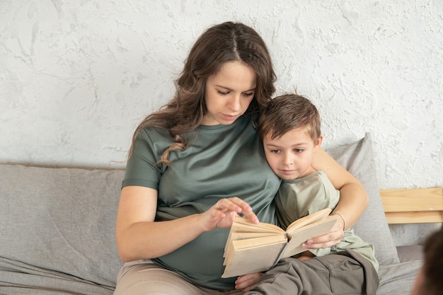 Menino aprendendo a ler um livro que a mãe o ajuda Família feliz sentada na cama Menino lendo um livro Conceito de passar um tempo juntos